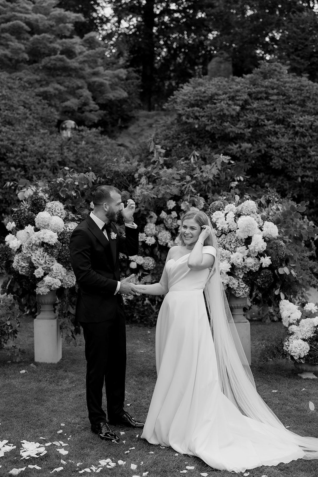 A couple shares romantic moments on a lawn outside a grand Victorian brick mansion with scattered white petals.