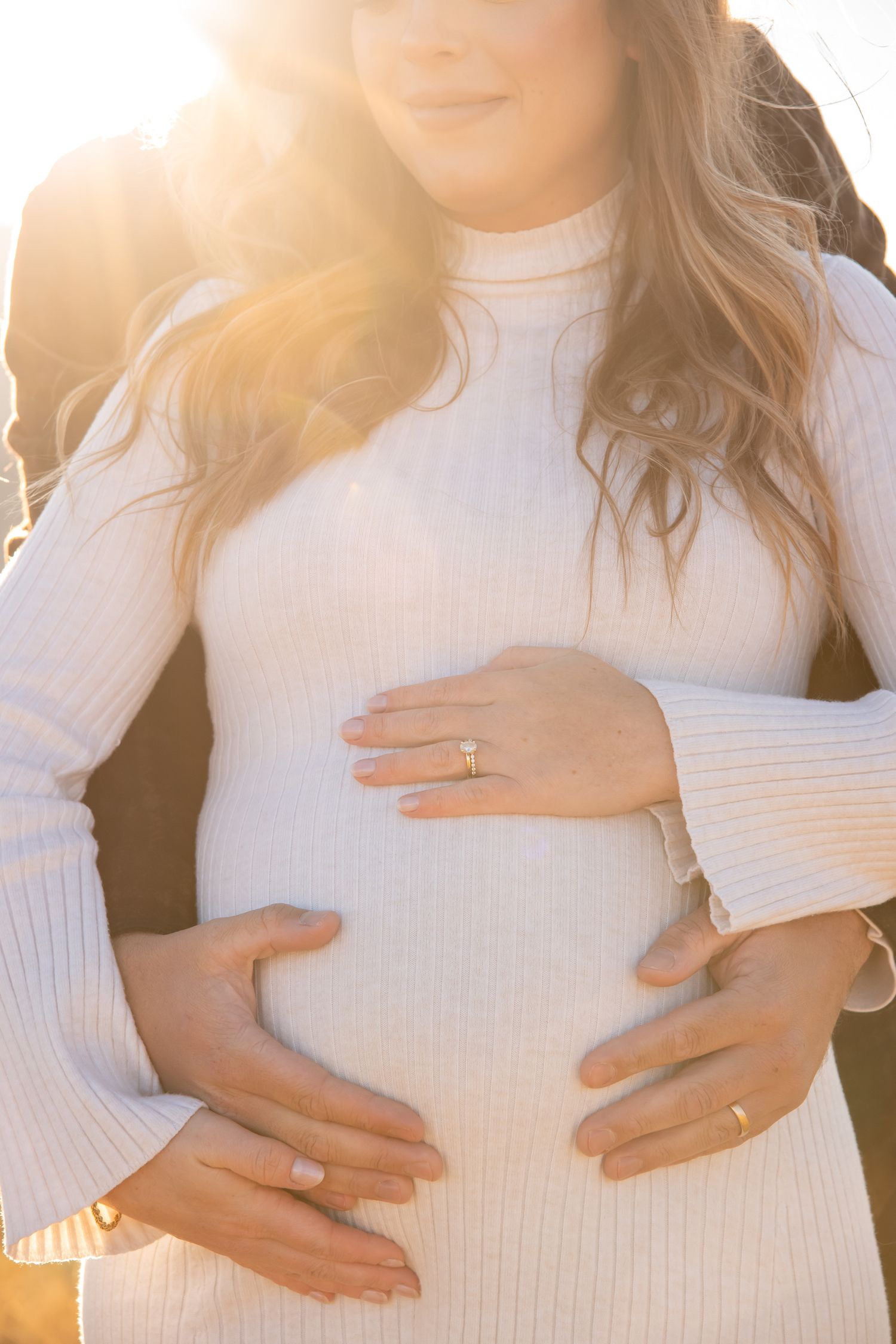 A close up image of hand holding a pregnant belly with golden light streaming in the background for a Vail Colorado maternity photo session