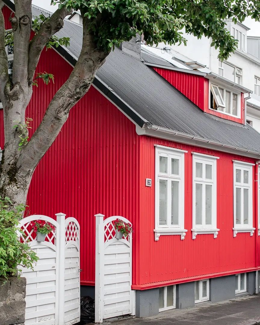 Red wooden house with white trim and a grey roof beside a tree.