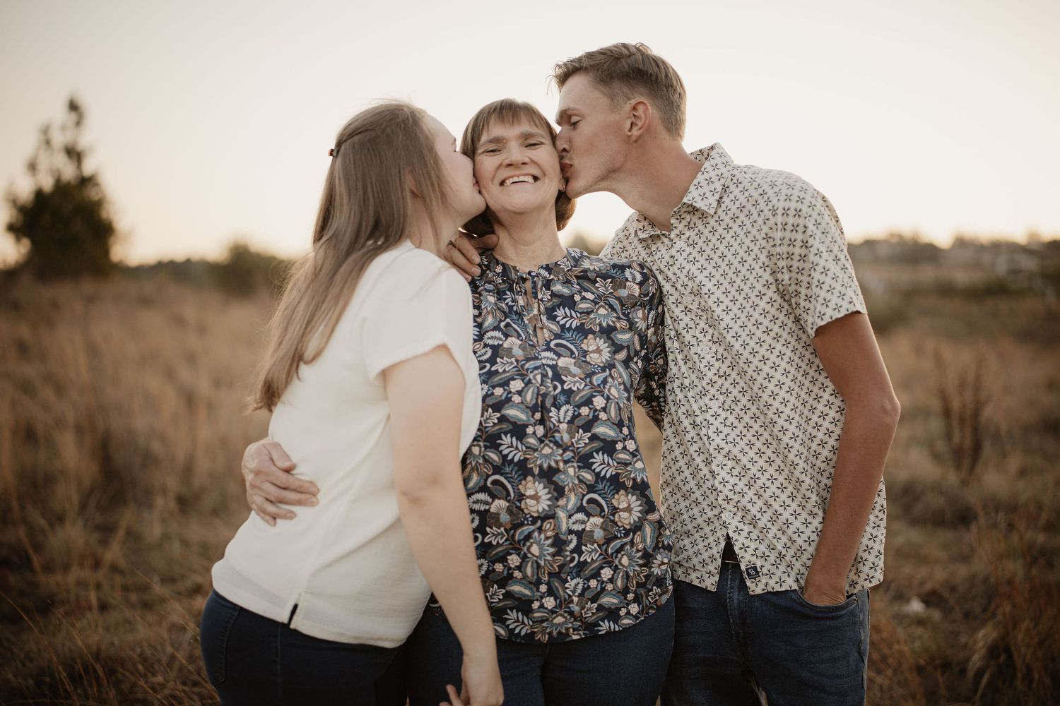 A couple embraces in a golden field during sunset while wearing casual attire.