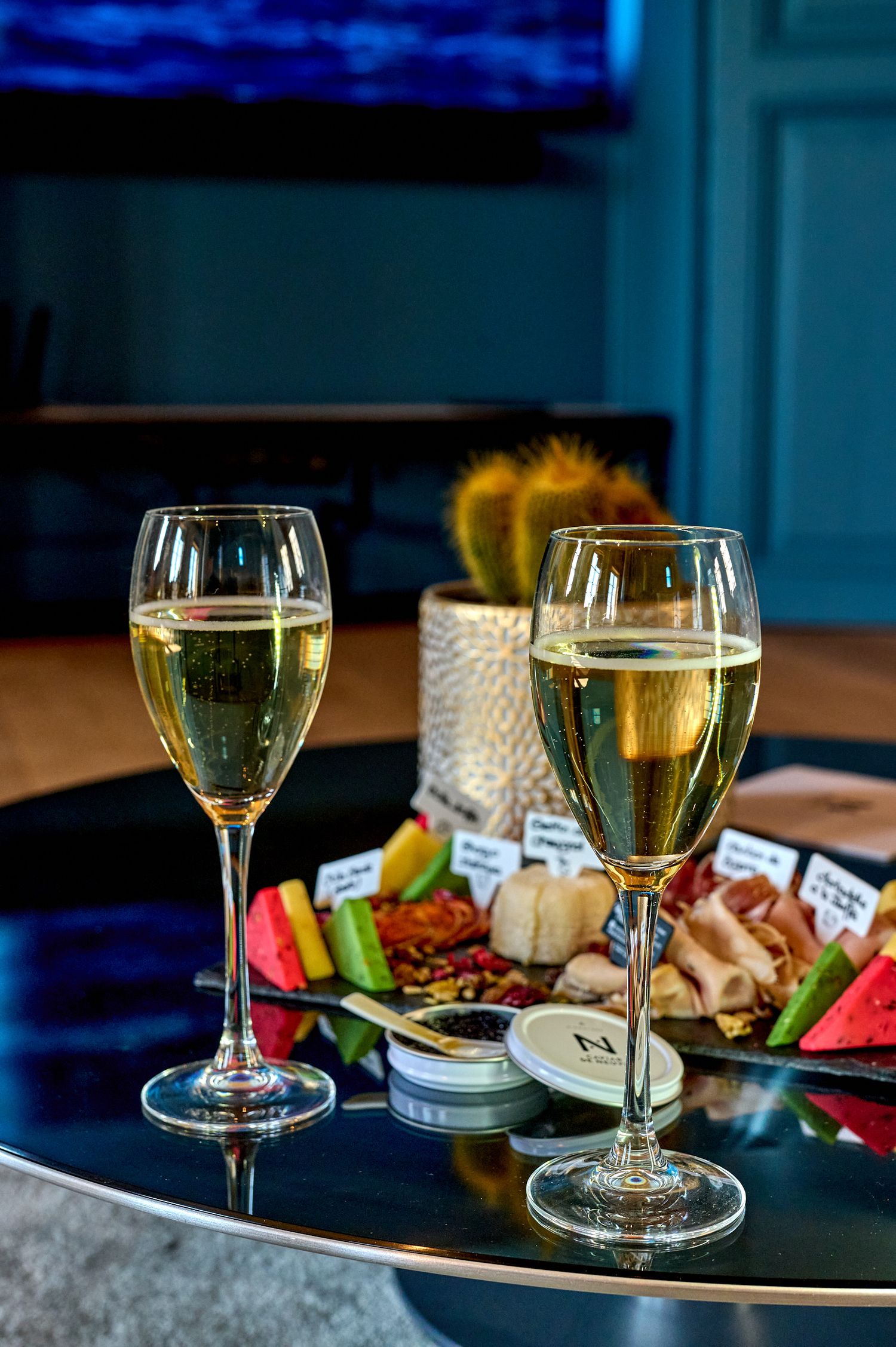 Elegant wine glasses with white wine alongside appetizer plates on a dark table with moody blue lighting.