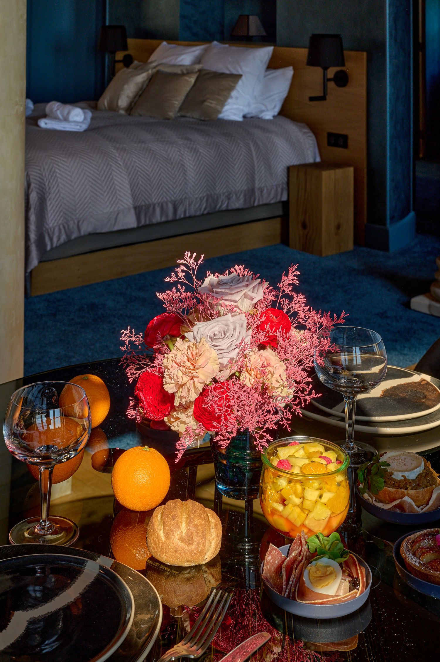 Cozy evening table setting with glowing candles, oranges, and pink coral decorations against dark moody lighting.