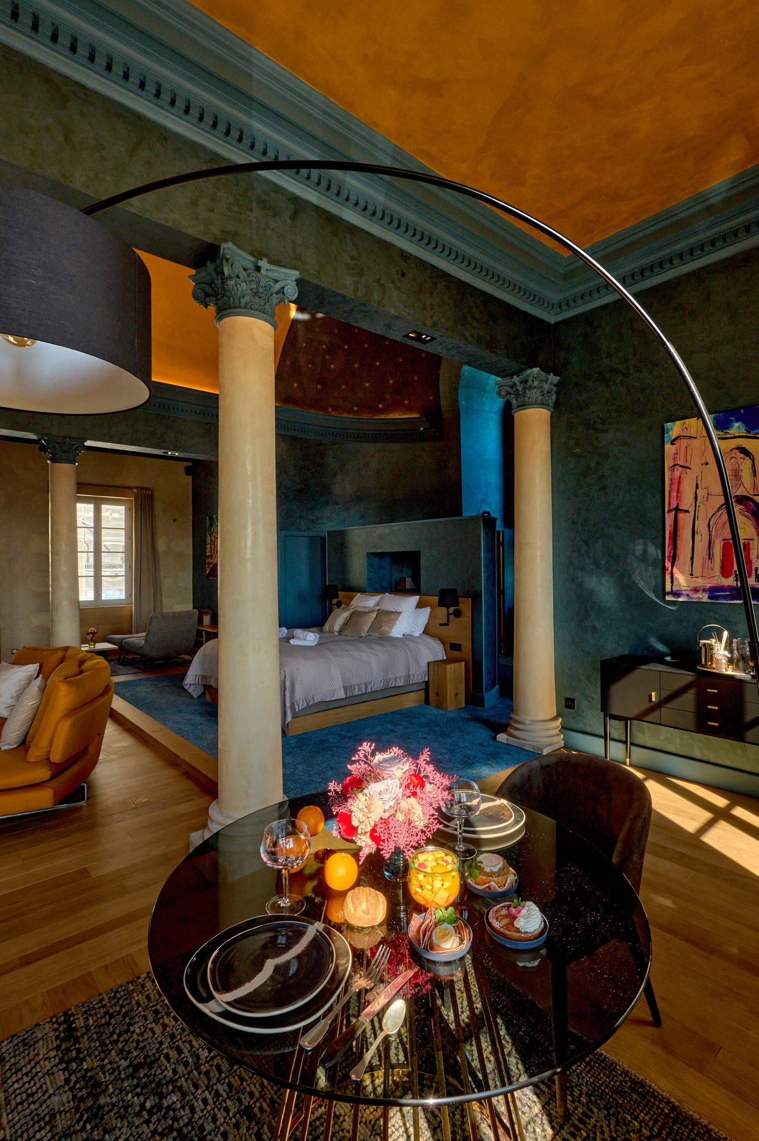 Luxury hotel suite with classical columns, hardwood floors, and mood lighting showcases elegant decor and dining setup.