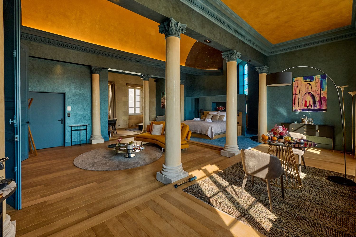 Panoramic view of an empty yoga studio with hardwood floors, blue walls, and natural light streaming through windows.