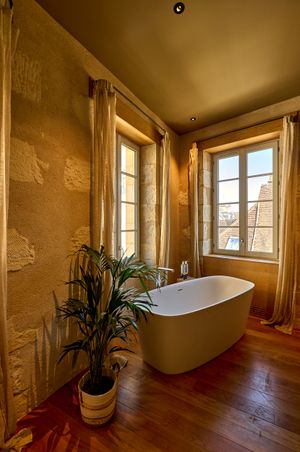 Modern freestanding bathtub sits elegantly in a sunlit bathroom with warm wooden floors and potted plants.