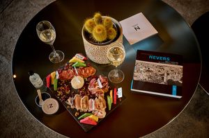 Elegant dinner setting with wine glasses, grilled meat platter, fresh vegetables, and a decorative postcard on dark table.