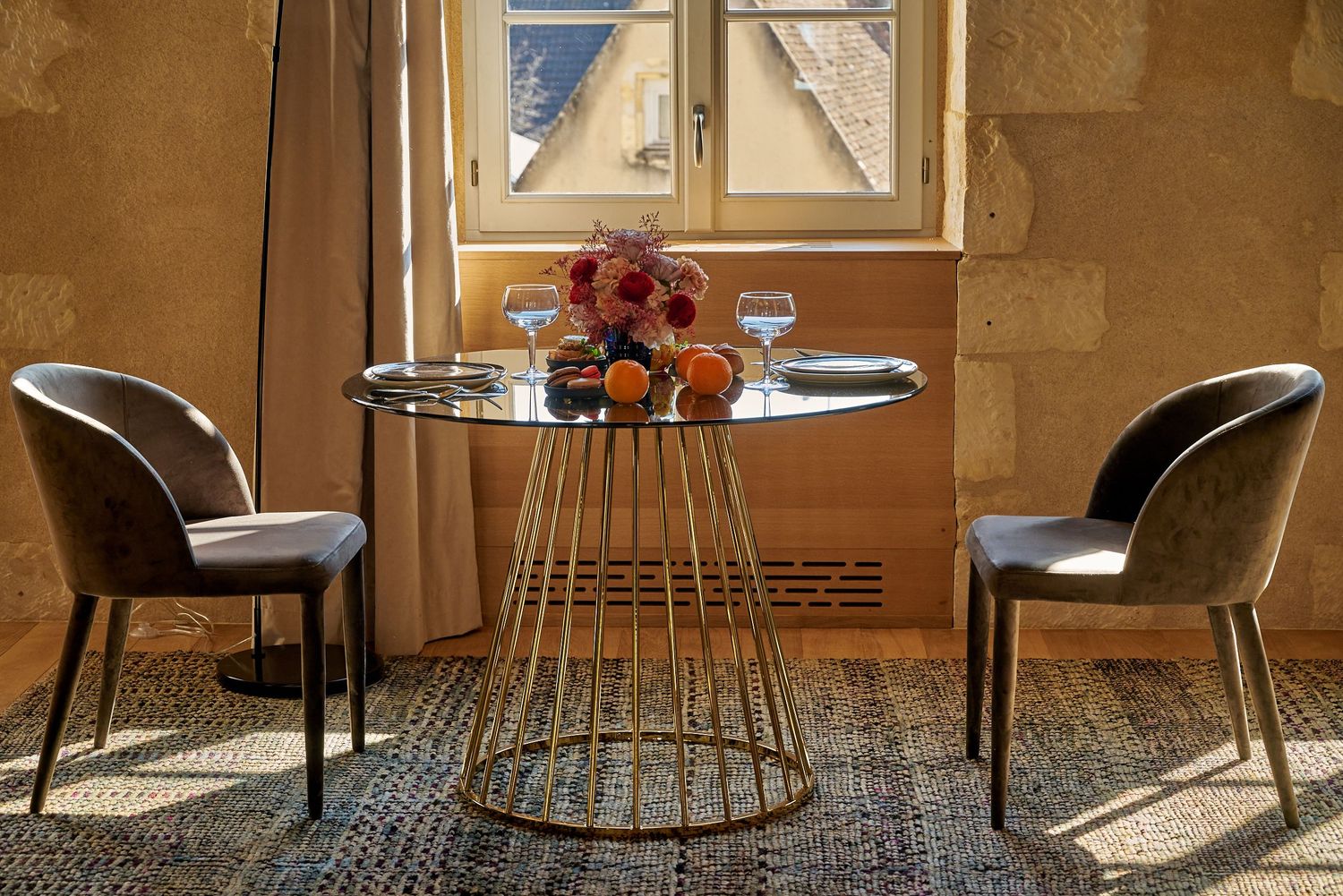Modern restaurant interior with upholstered gray chairs and round glass tables against textured beige walls.