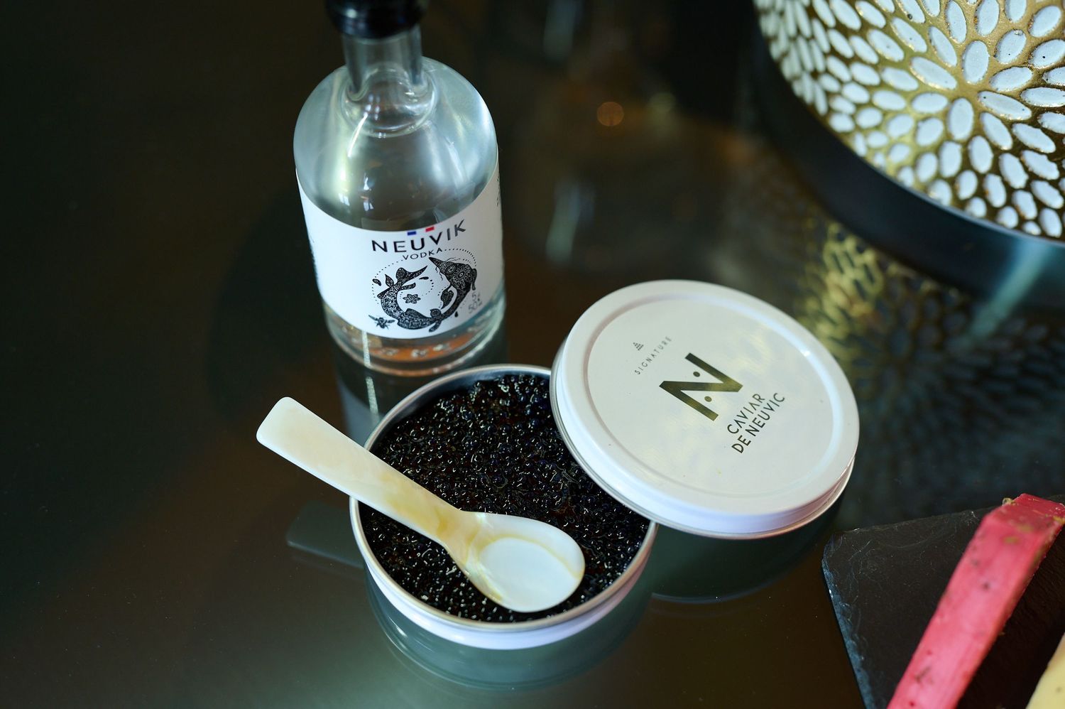 Caviar being spooned onto a small serving plate with garnishes and accompaniments in a dark, elegant setting.