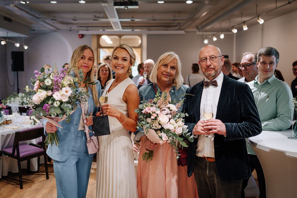 A wedding party poses together in a modern art gallery space with white walls and track lighting.