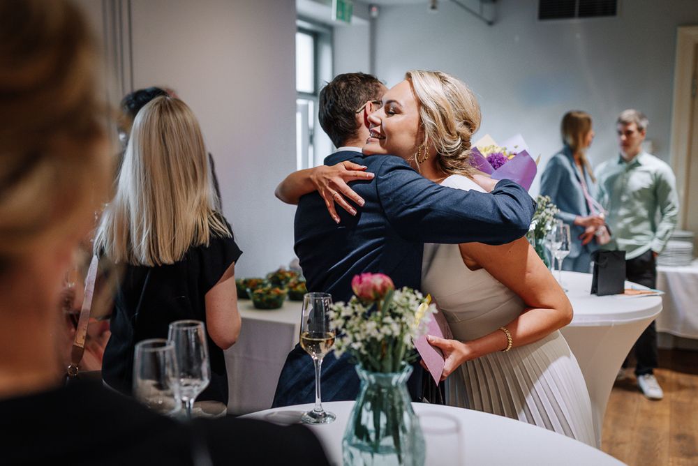 A couple embraces during a romantic moment at an indoor event with floral decorations and soft lighting.