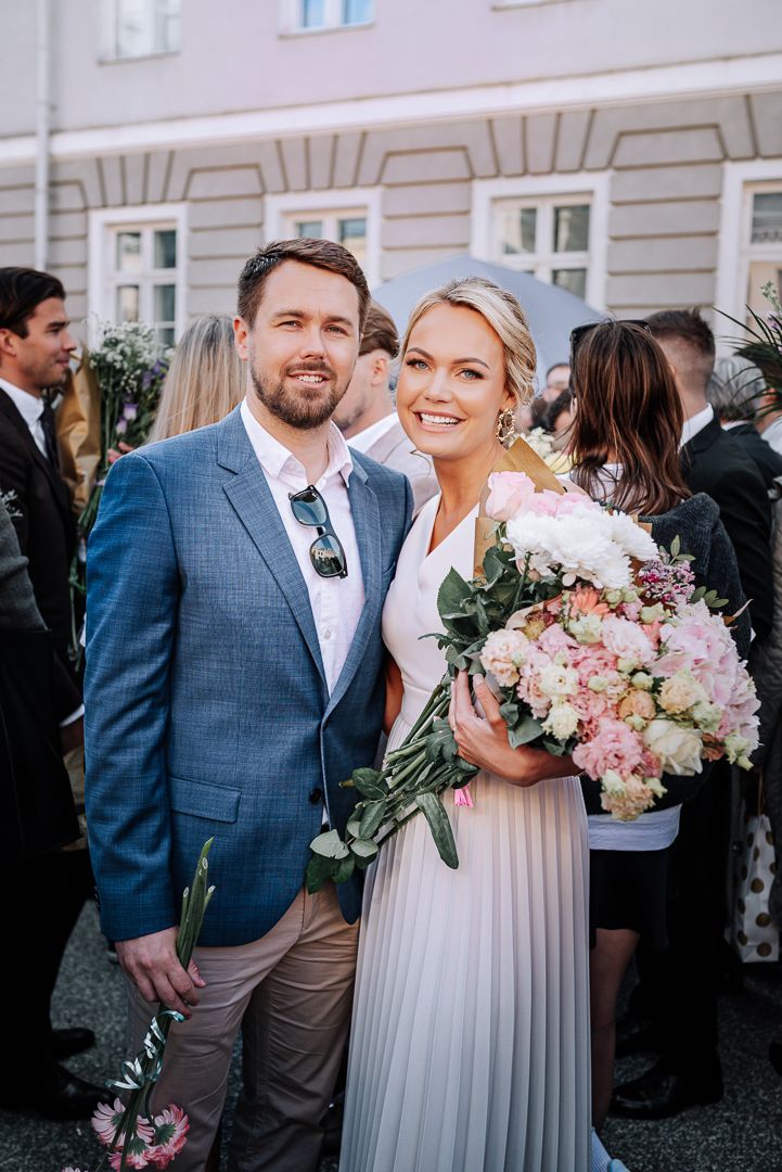 Wedding celebration with couple sharing joyful moments in a courtyard surrounded by guests and pink floral bouquets.