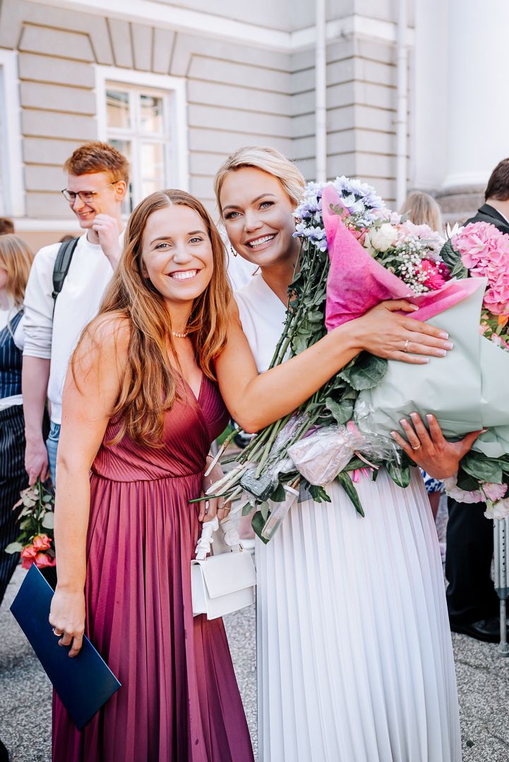 A group of wedding guests gather together with pink and white floral bouquets in an outdoor setting.
