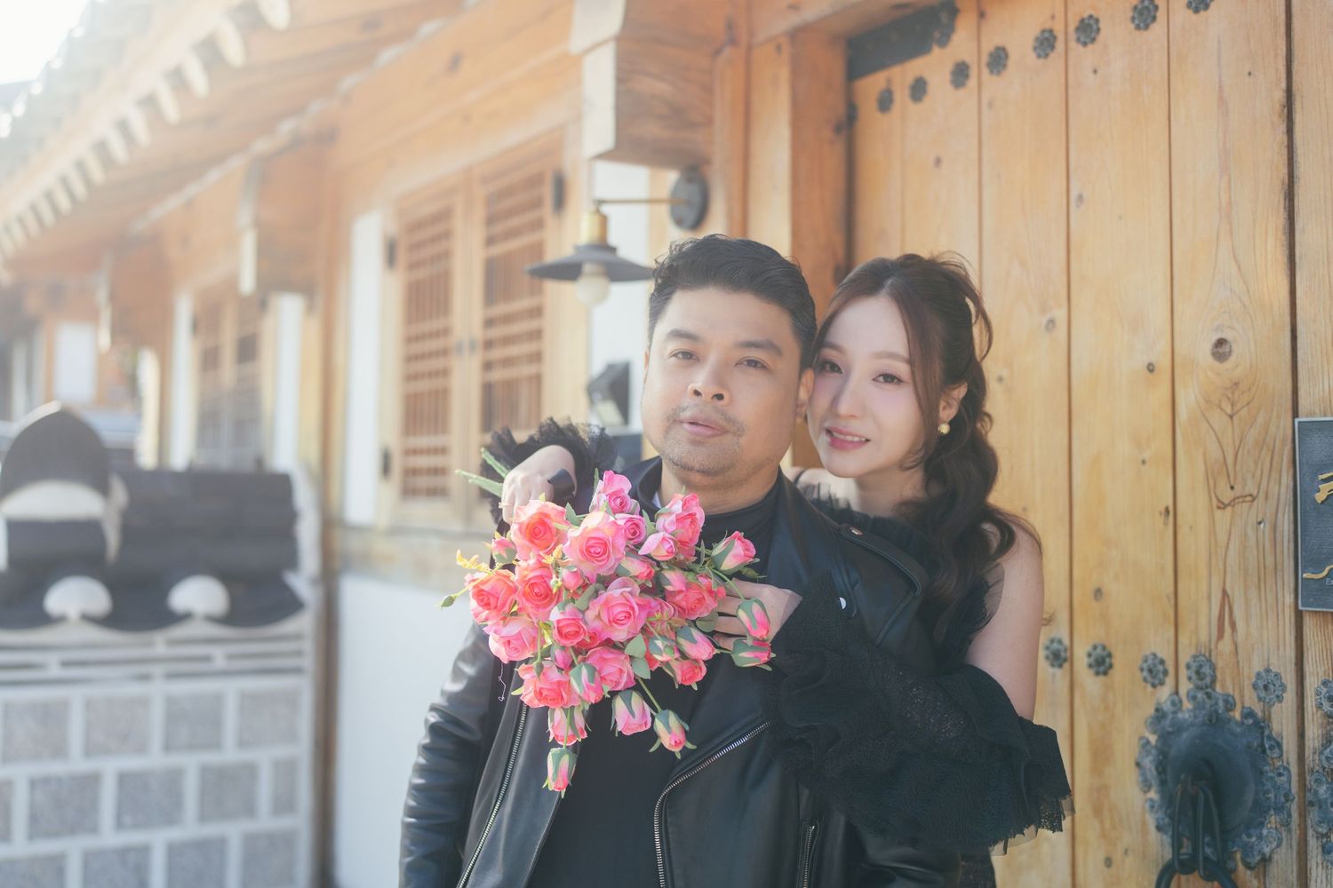 A couple poses in traditional Korean hanbok attire in front of a wooden door at a historic palace.