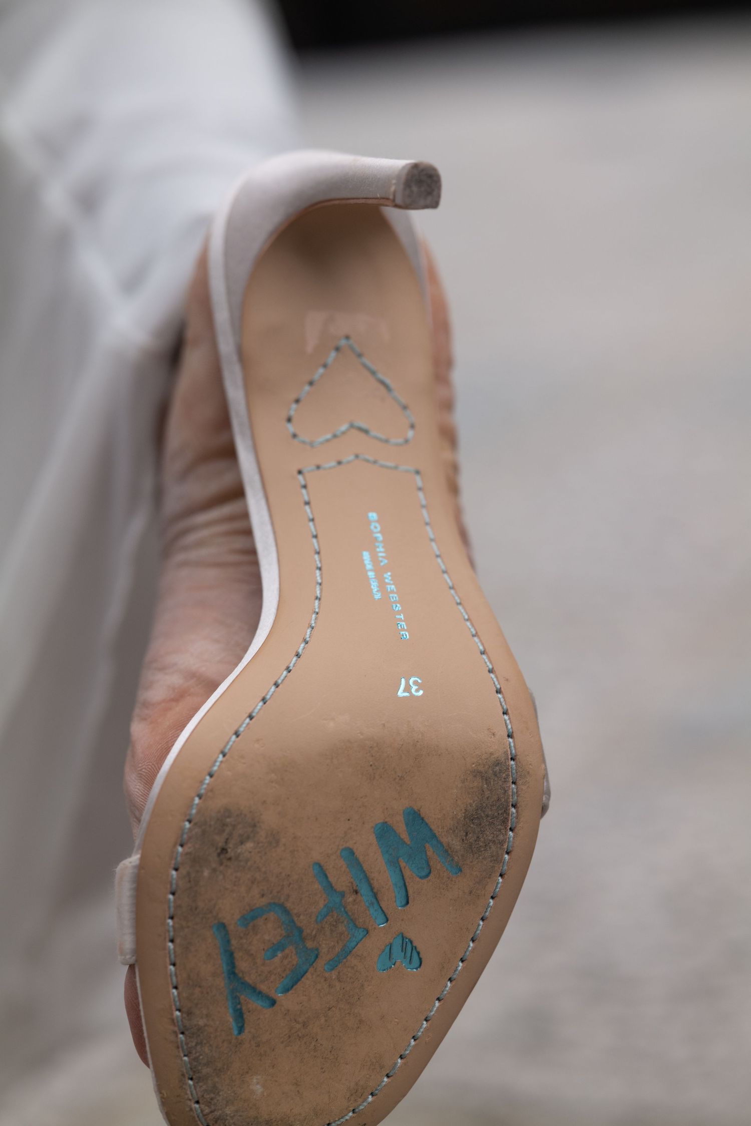 Bottom of a bridal heel shoe with WIFEY written in blue letters, size 37, on a cobblestone surface.
