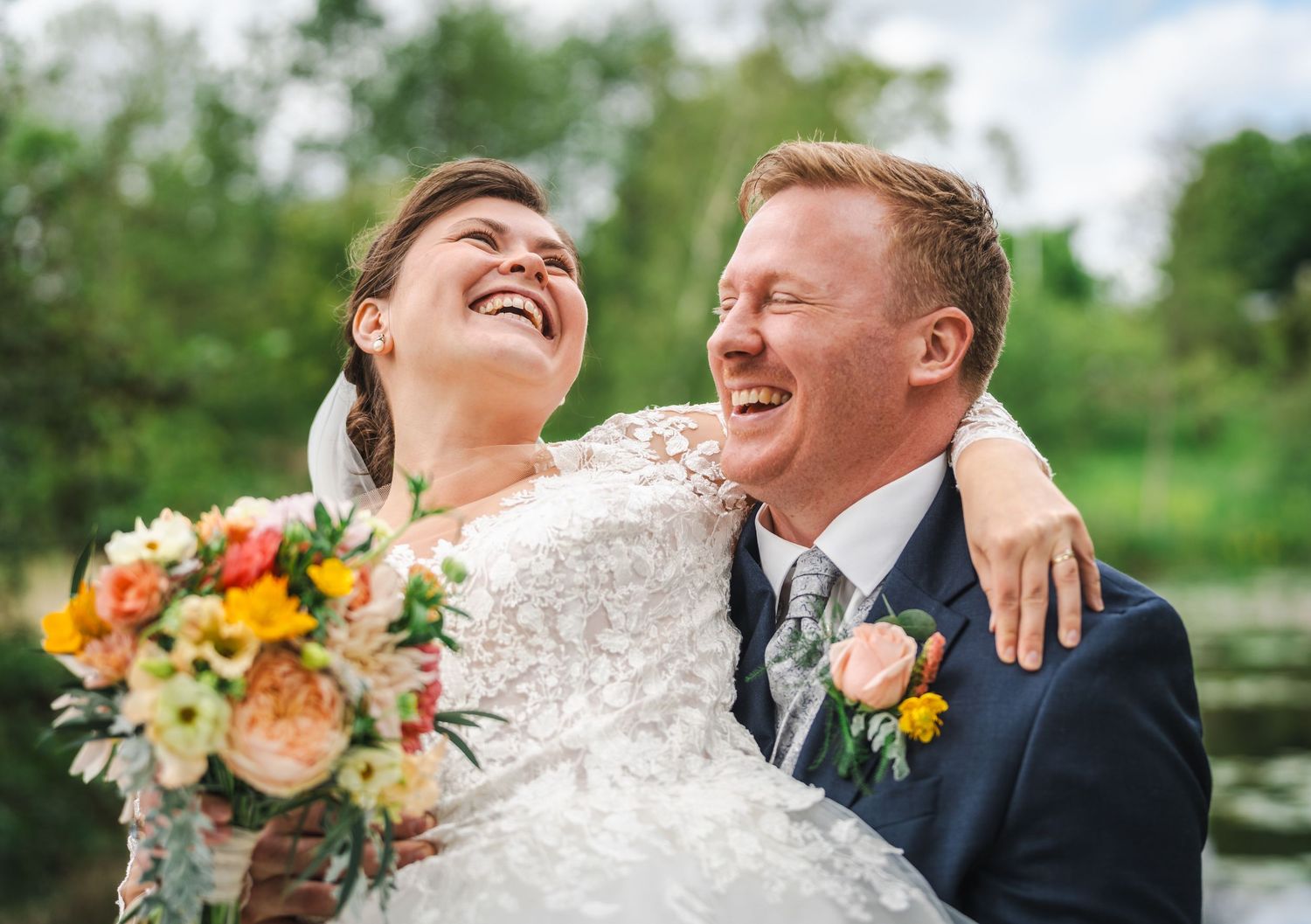 Joyful couple laughing together during outdoor wedding photoshoot with lush greenery in background.