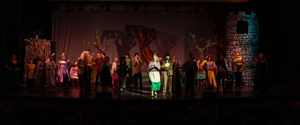 Theater performers on stage during a musical production with dramatic lighting and costumes.