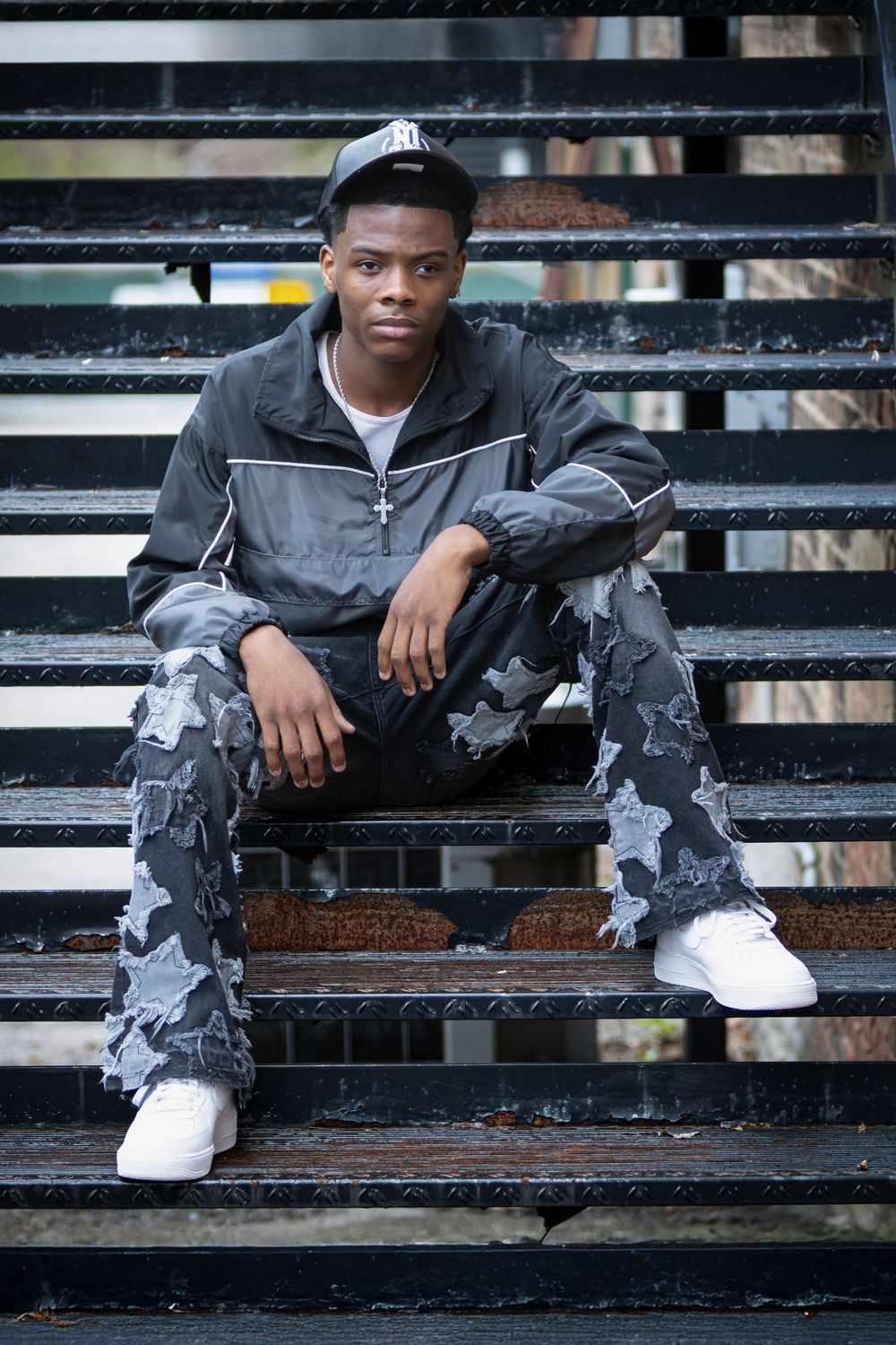 Person sitting on black steps wearing grey and white urban streetwear.