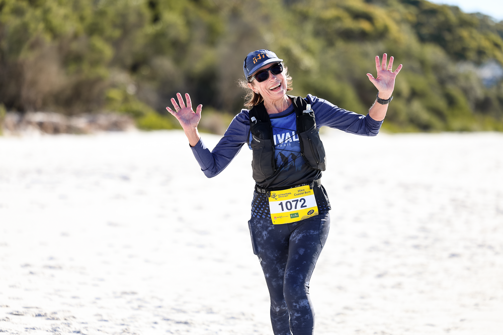 Female runner wearing bib number 1072 celebrates with raised hands during an outdoor trail race event.