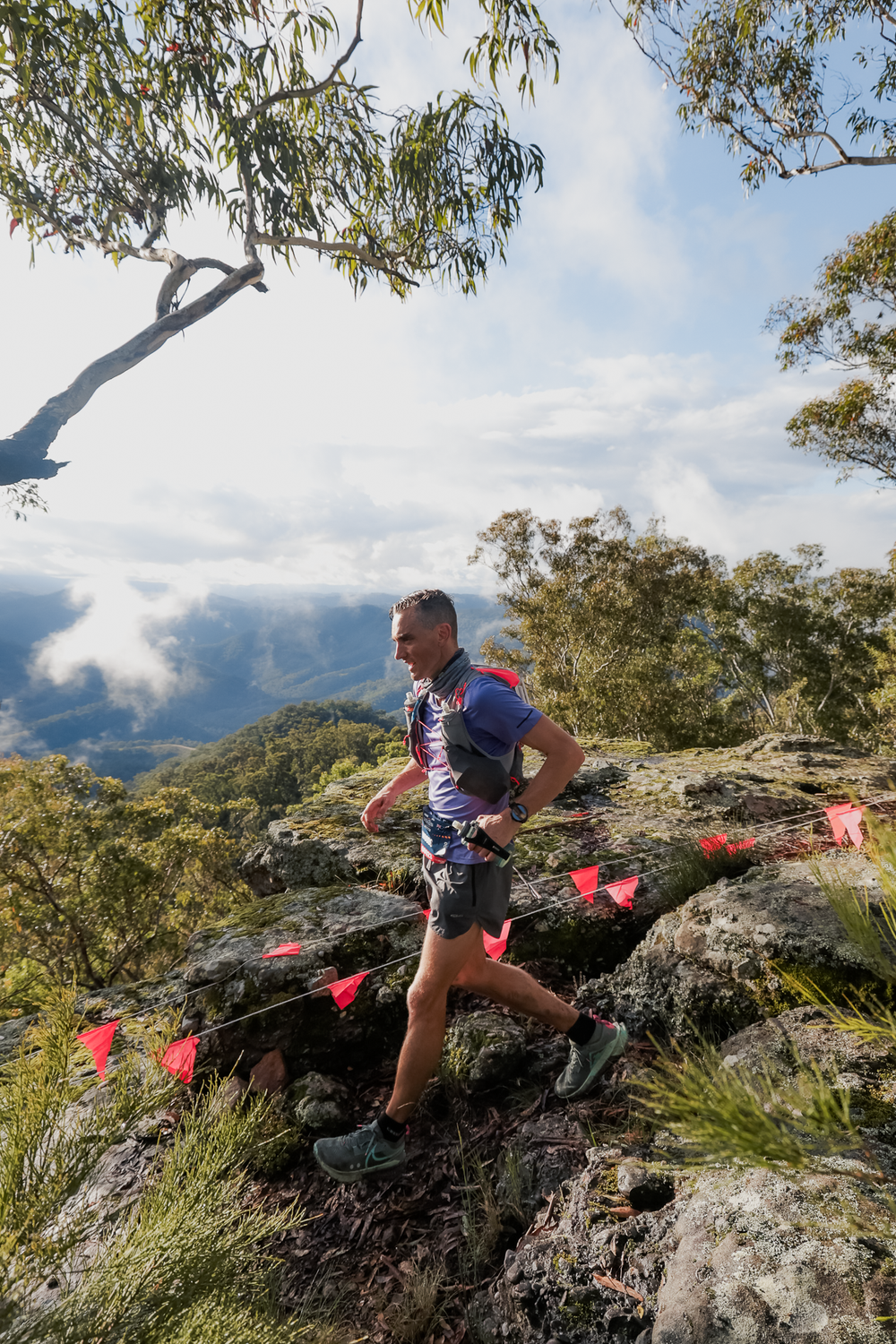 Trail runner navigating rocky mountain terrain with red flags marking the course and scenic valley views below.