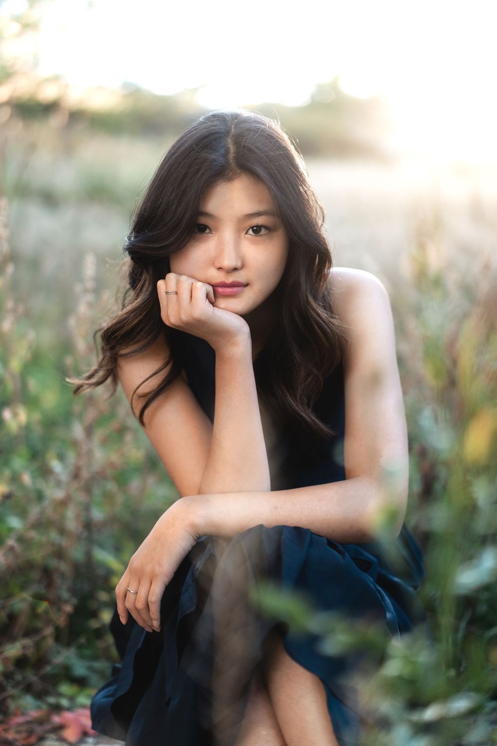 A woman in a black dress poses thoughtfully among wildflowers during golden hour.