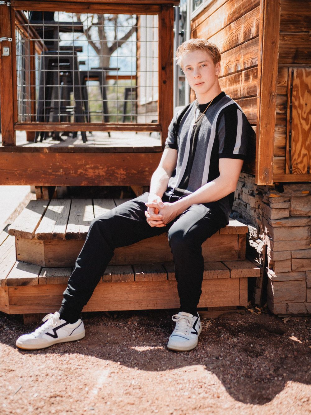 Athletic person in black and white striped shirt and pants sits on wooden porch steps in bright sunlight.