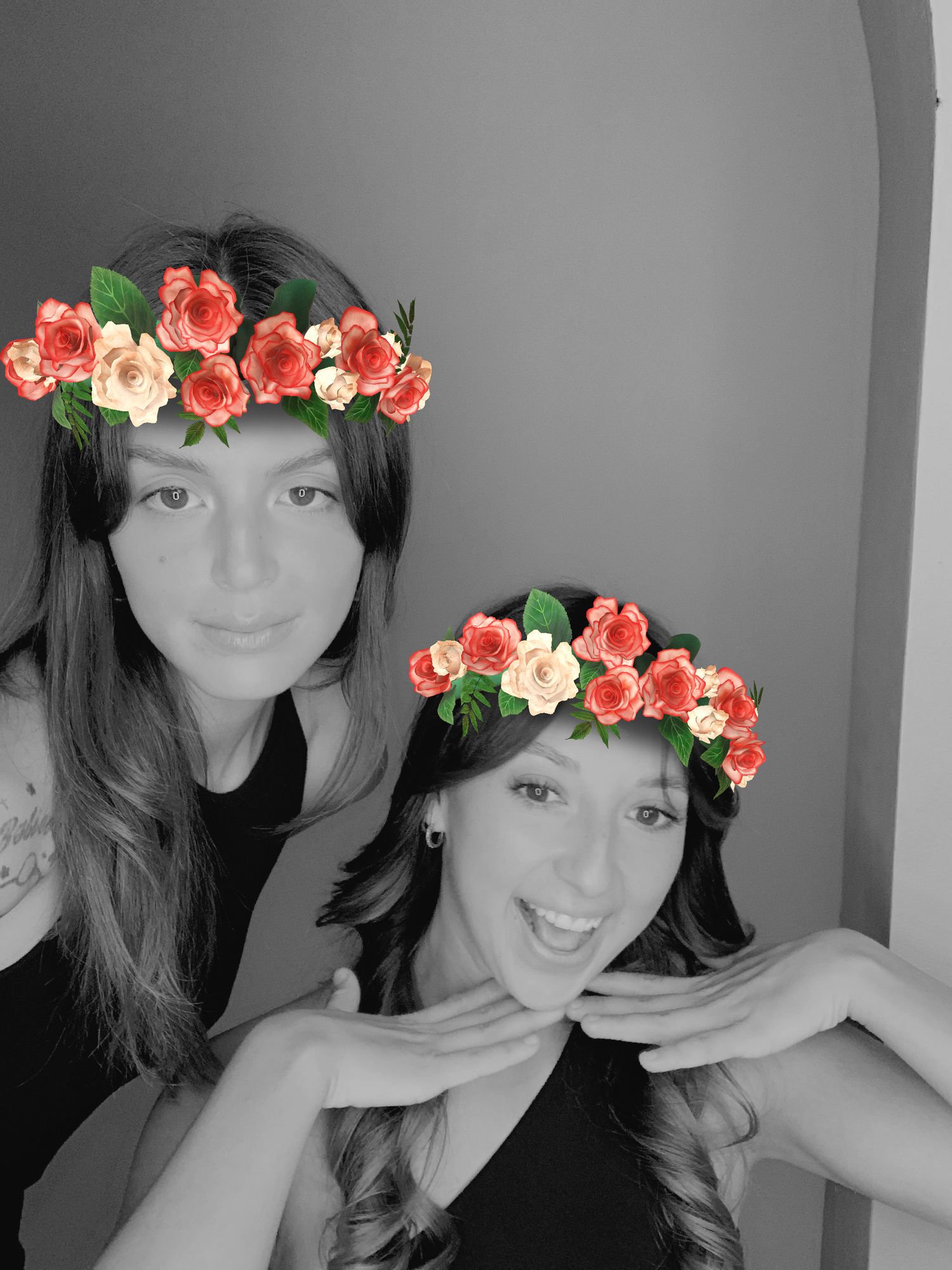 Black and white photo of two people wearing colorful floral crowns made of coral and cream roses.