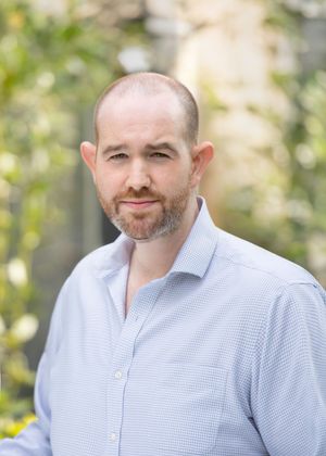 A series of four similar headshots showing a person in a light blue button-down shirt against a blurred outdoor background.