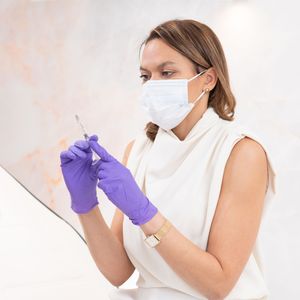 Medical professional in protective gear examining samples in a clinical laboratory setting.
