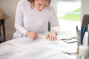 Person in white long sleeve shirt writing notes on paper at bright desk surface.