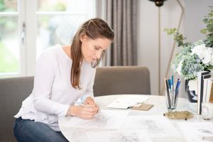 Woman in white shirt working at desk with laptop and papers in bright modern office space.