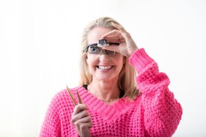 Someone wearing a bright pink knitted sweater smiles while holding a nail file against a white background.