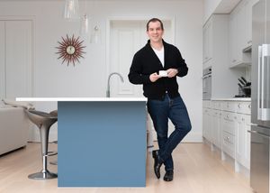 Person in business attire poses with blue furniture piece against white modern interior.