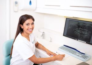 Healthcare worker in white uniform working at computer workstation in medical office.