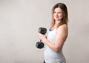 A person in a white tank top holds a black dumbbell while working out against a light gray background.