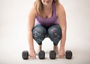 Person in purple tank top performing dumbbell workout on white background.
