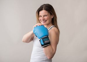 Woman in white tank top demonstrates four boxing stances while holding blue boxing gloves.