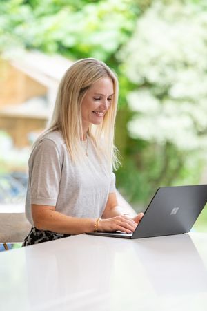 Professional working on a laptop outdoors with natural greenery and bokeh background in summer setting.
