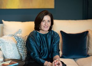 Woman in dark blue top relaxes on a contemporary sofa with decorative pillows in warm lighting.