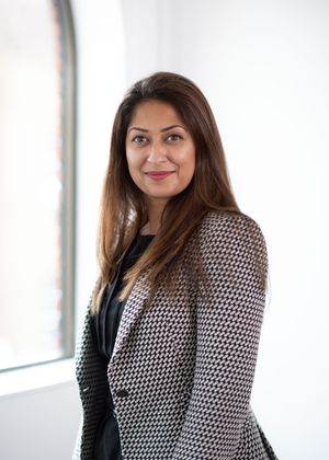 Professional portrait of someone wearing a polka dot blazer and black top standing near a window.