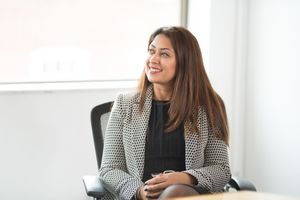 Professional woman in black and white checkered blazer sits at desk in modern office setting.