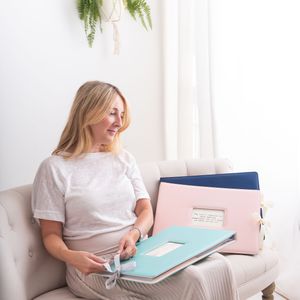 Pregnant woman in white loungewear relaxes with documents and folders while sitting on cozy couch at home.