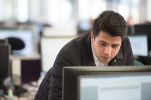 A person sits at a desk working intently on a computer monitor in an office environment.