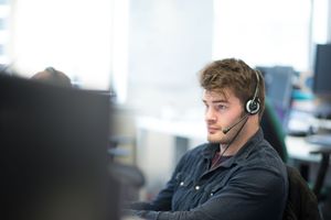 A group of customer service representatives wearing headsets work at computer stations in a modern office setting.