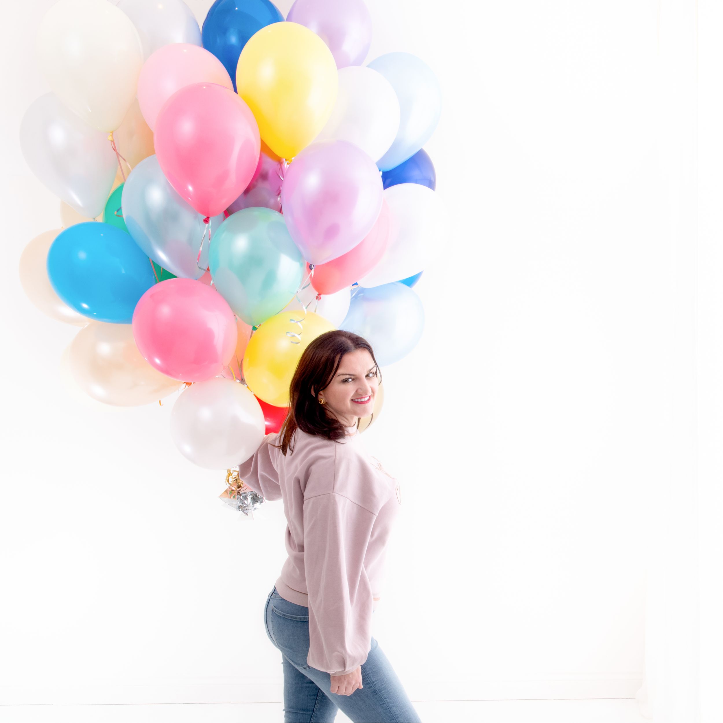 Woman in pink sweater dancing joyfully with colorful balloons against white background in sequence shots.