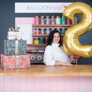 Festive party setup with balloon bar display featuring gold number balloons and pink decorative elements on wooden table.