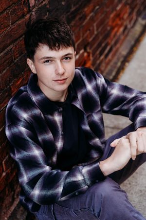 Portrait series against brick wall showing young person in plaid flannel shirt and dark pants in casual poses.