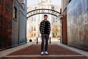 A person stands in a brick alley with an arched entrance and converging walls creating dramatic perspective.