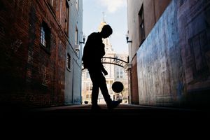 A silhouetted figure walks through a narrow urban alleyway with dramatic lighting and brick walls.