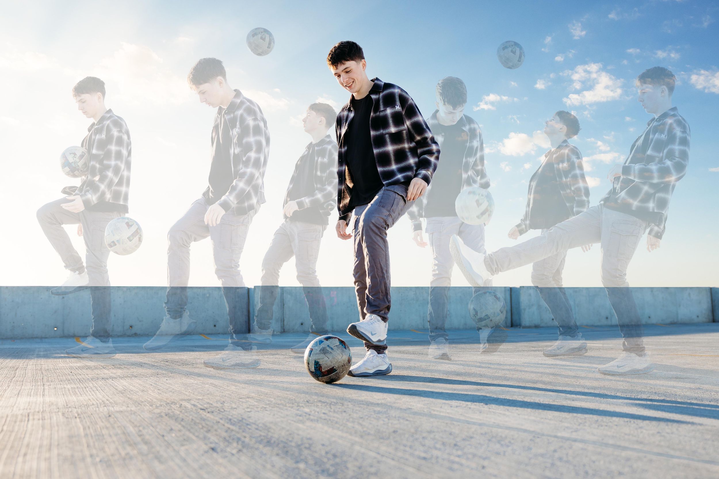 A person performs soccer freestyle tricks with a ball on a sunny outdoor court with shadows visible.