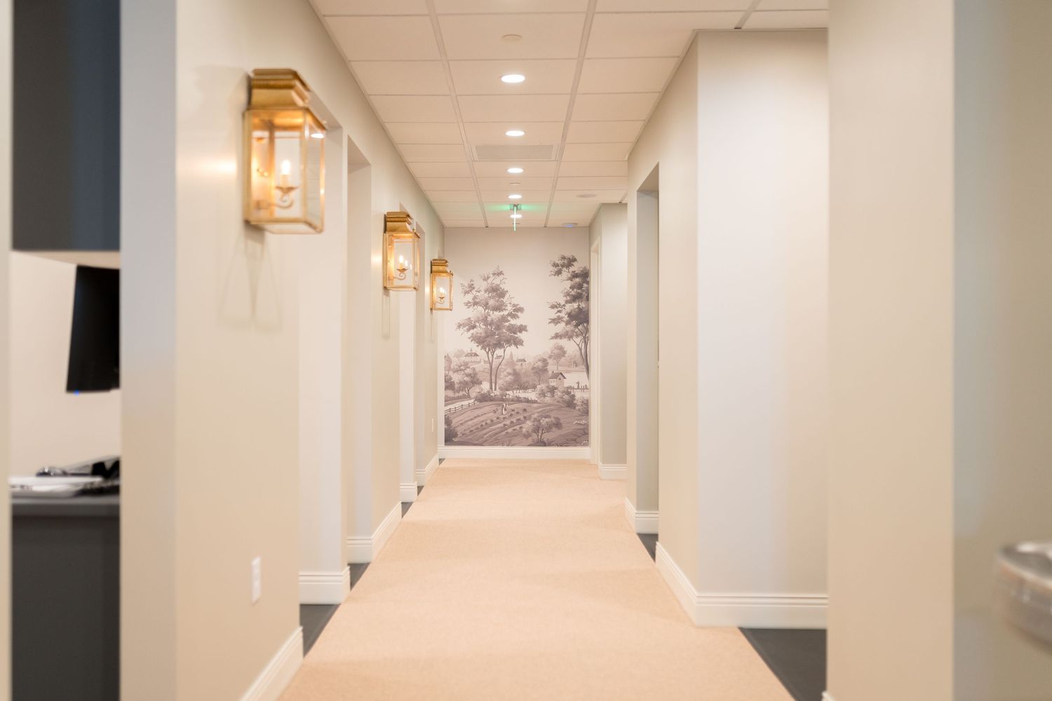 Long hallway in a medical facility with white walls and warm lighting fixtures.